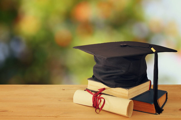 Image of graduation black hat over old books next to graduation on wooden desk. Education and back to school concept - Zdjęcie, obraz