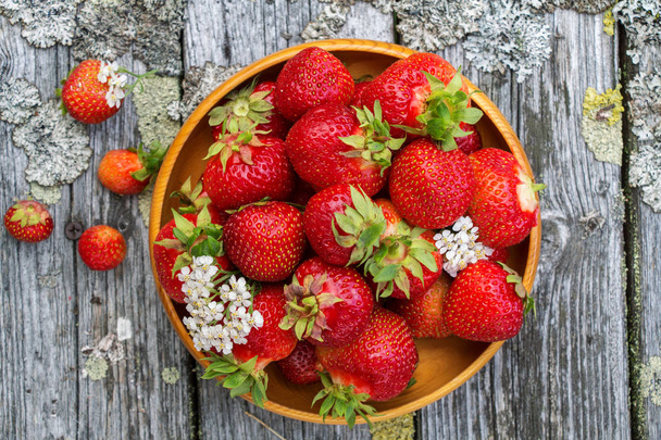 Red ripe strawberries in a wooden basket on the old boards on the background of green grass - 写真・画像