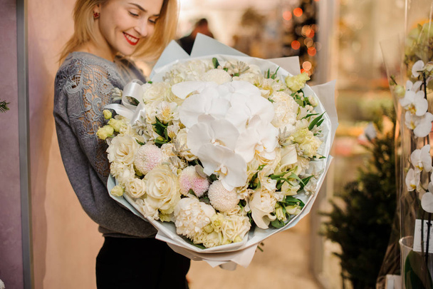 blonde female smiles and holds a bouquet with white orchids, eustoma, kraspediya, white roses - Photo, image