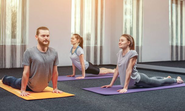 Zwei schöne Mädchen und ein Mann machen Yoga im Sportzentrum und im Wellnessbereich. das Konzept eines gesunden Lebensstils. - Foto, Bild