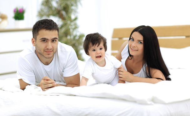 Portret van gelukkige jonge familie samen in bed liggen - Foto, afbeelding