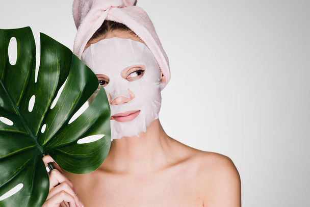 young girl with a pink towel on her head, on her face a tissue moisturizing mask, day spa - Foto, Imagen