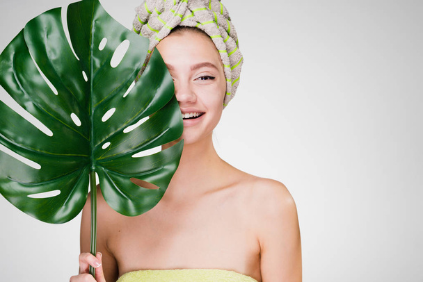 happy smiling girl with a towel on her head holds a green leaf, day spa - 写真・画像
