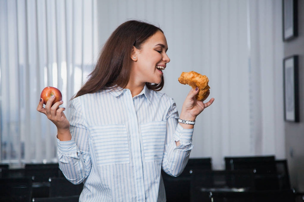Healthy food or junk food choice concept. Attractive woman hold red apple and croissant - Fotó, kép