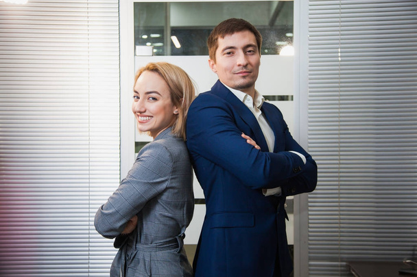 Two respectable business people in formal suits stand together. Man and woman at office room pose to camera. Teamwork, cooperation, success concept - Foto, Bild