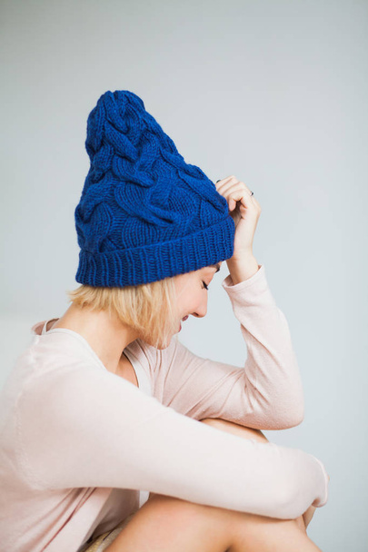 Nuori nainen lämpimässä tummansininen käsi neulottu hattu kotona. Kaunis nainen iso sininen lakki, hymyillen onnellisena. Pystysuora laukaus
. - Valokuva, kuva