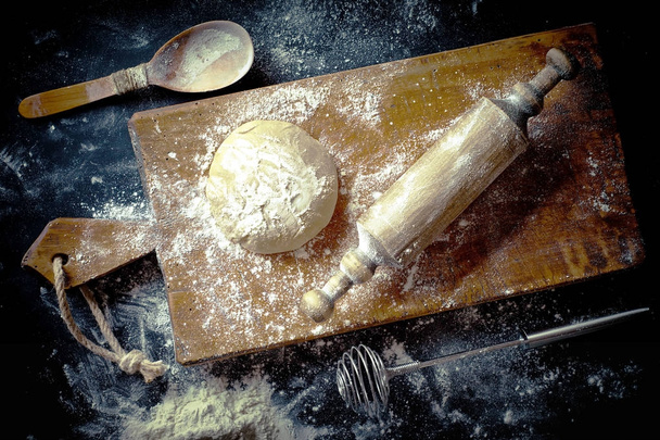 Testo con harina sobre un fondo viejo en una composición con accesorios de cocina
 - Foto, Imagen