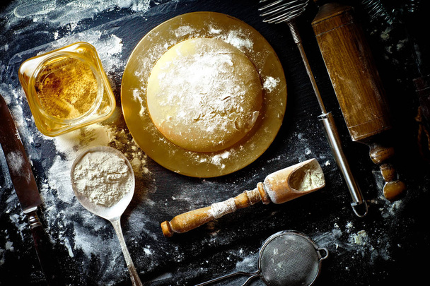 Dough with flour on an old background in a composition with kitchen accessories - Photo, Image
