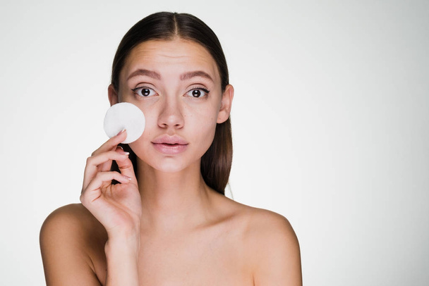 a cute young girl looks after the skin on her face, holds a white cotton pad to cleanse the skin on her face - Foto, imagen