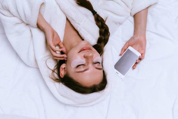 a young girl in a white terry dressing gown is lying on the bed, sleeping, in her hand the phone - Foto, imagen