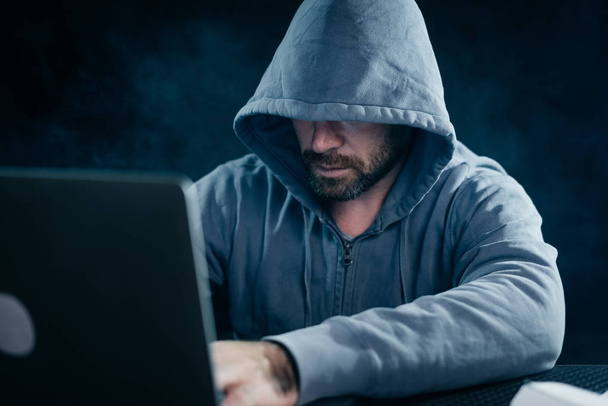 mysterious bearded man hides his face under the hood, hacks the laptop - Foto, Imagem