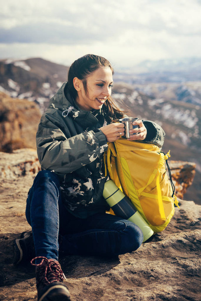 happy young girl sitting on the edge of a cliff, drinking hot tea and enjoying nature - Photo, Image