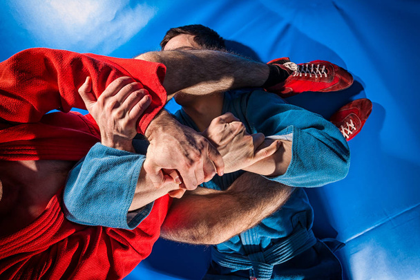 Крупним планом двоє борців за пастку і джу дзіцу в синьому і червоному кімоно роблять мушкет. Реслінгова боротьба синіх татамі
 - Фото, зображення