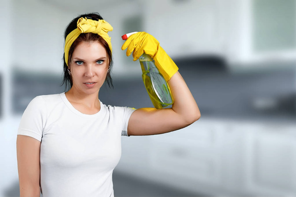 The girl, the cleaning lady after cleaning, stands with a displeased face, holding a cleaning agent in her hands on a blurred background. The concept of cleanliness in the house, cleaning the premises - Foto, Imagen