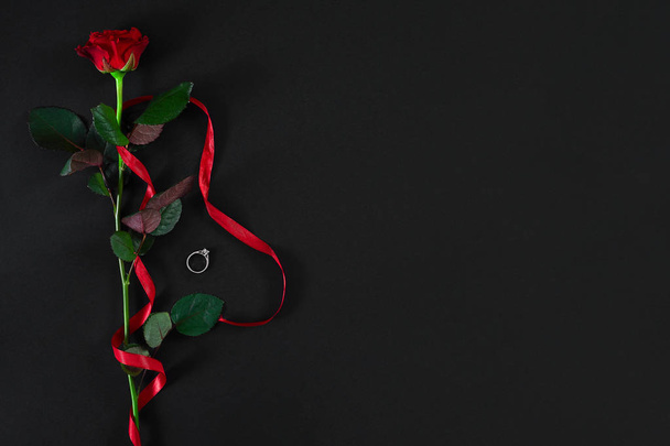 Uma rosa vermelha escura com fita vermelha e o anel no backgrou preto
 - Foto, Imagem