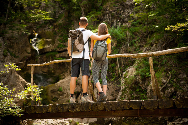 active young cople hiking on a wooden brifge over mountain creek - Zdjęcie, obraz