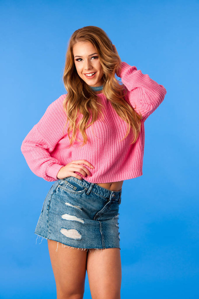 Beautiful young woman in pink sweater and jeans dance over vibrant blue background  - Photo, image