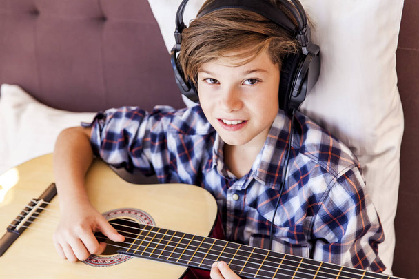 Teenage boy playing acoustic guitar in bed - Photo, Image