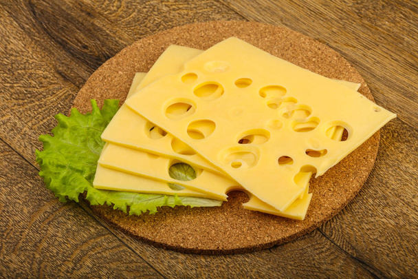 Szeletelt sajt saláta levelek fölött a fából készült háttér - Fotó, kép