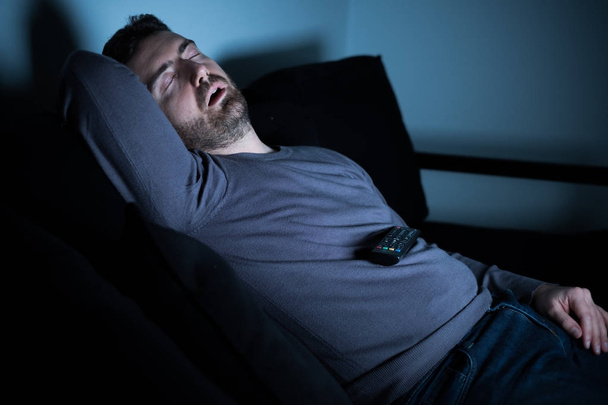 Hombre durmiendo en el sofá delante de la pantalla de televisión
 - Foto, imagen
