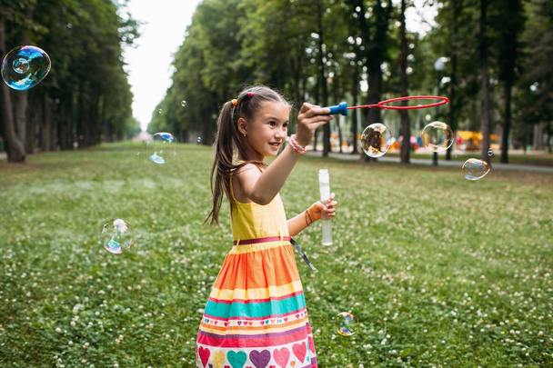 Εντυπωσίασε το μικρό κορίτσι φυσάει φυσαλίδες στο πάρκο. - Φωτογραφία, εικόνα