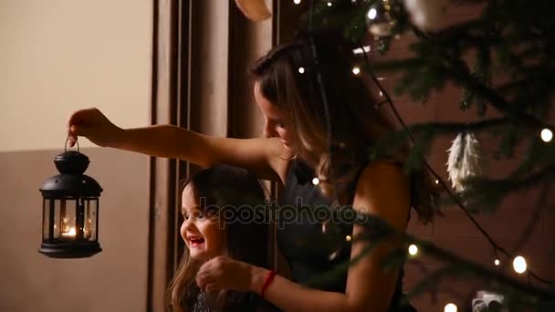 Mutter und Tochter entzünden eine Taschenlampe mit einem lebendigen Feuer unter dem Weihnachtsbaum und das Mädchen bläst eine brennende Kerze aus. - Filmmaterial, Video