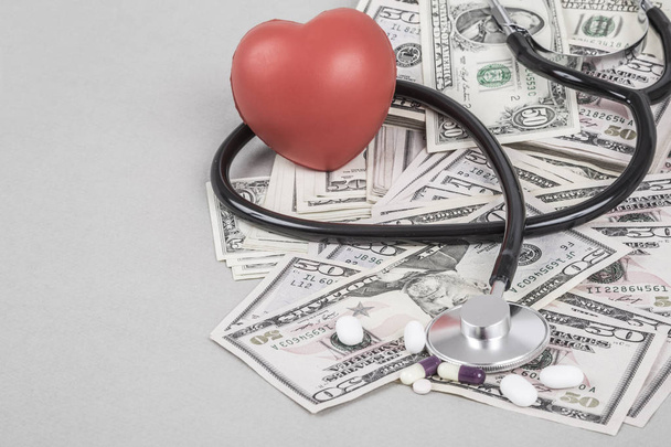 Un estetoscopio y un corazón rojo sobre dólares americanos sobre fondo gris
 - Foto, Imagen