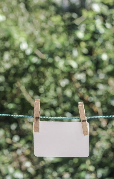 papel blanco vacío colgado con clavijas de ropa en la cuerda en el jardín
 - Foto, Imagen