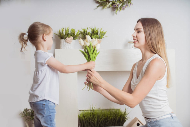 Feliz dia da mãe! A filha da criança parabeniza a mãe e dá-lhe flores tulipas. Mãe e menina sorrindo e abraçando. Férias em família e união
. - Foto, Imagem