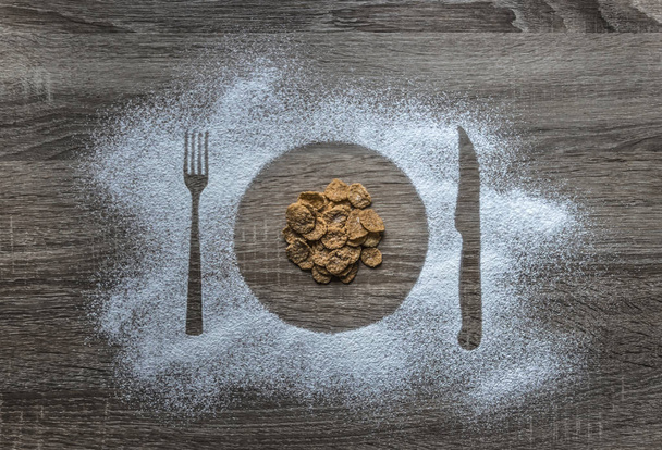 on a wooden background flour powder powdered snow silhouette plate plate fork knife appliances in the center poured corn cereal flakes  - Fotoğraf, Görsel
