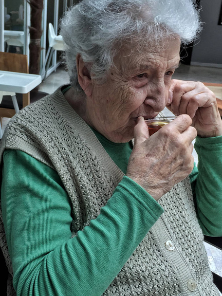 vanhempi nainen juo lasillisen teetä
 - Valokuva, kuva