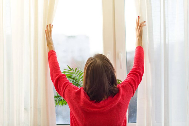 Woman looks out the window, opens the curtains. - Foto, Imagem