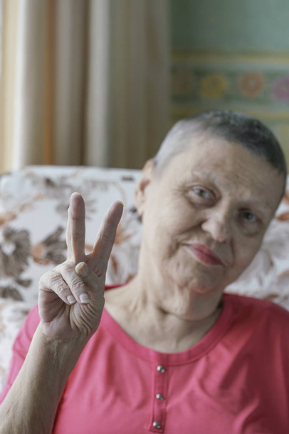 Old happy cancer survivor woman doing victory sign after successful chemotherapy - Photo, Image