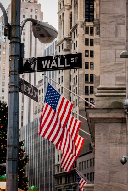 Сосредоточьтесь на табличке Уолл-стрит в Нью-Йорке с американскими флагами на заднем плане
 - Фото, изображение