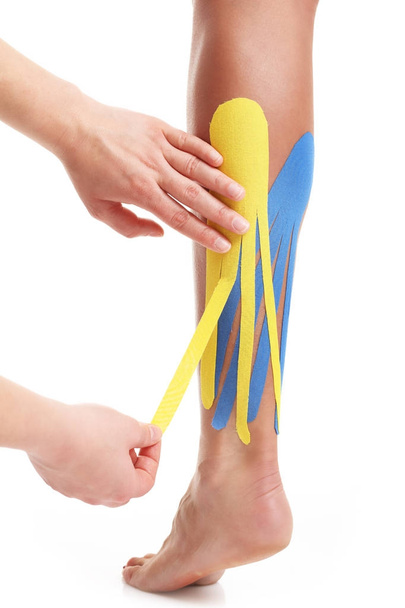 Obrázek ukazující speciální fyzioterapie pásku vložit na zraněné tele nad bílým pozadím - Fotografie, Obrázek