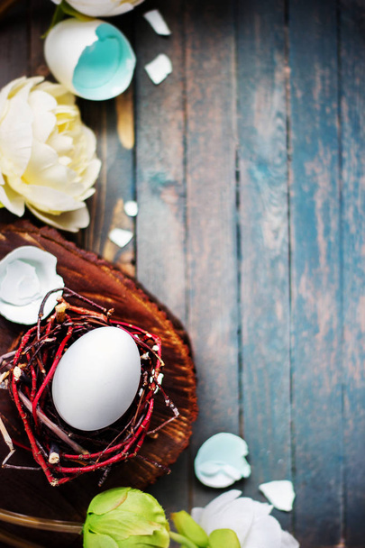 White egg in little nest with light flowers on wooden rustic background. Easter spring concept - Fotó, kép