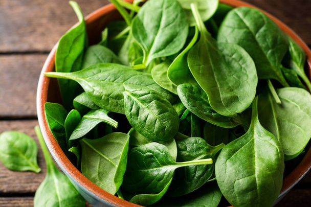 Fresh spinach leaves in bowl on rustic wooden table. - Foto, afbeelding