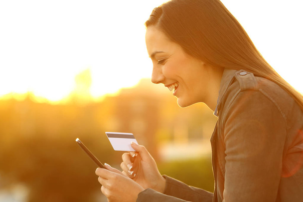Girl buying on line with credit card at sunset - Photo, Image