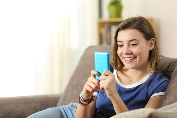 Teen using a blue smartphone at home - 写真・画像