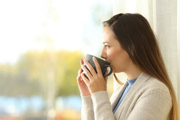 女性コーヒーを飲むと、窓から見て - 写真・画像