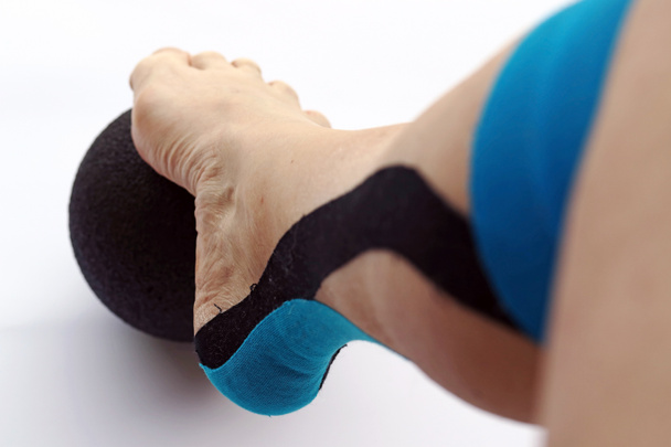 Een vrouw met een tape pleister op haar been doet bewegingsoefeningen. Kinesio tape op de been. Tape plakband voor sportgeneeskunde - Foto, afbeelding