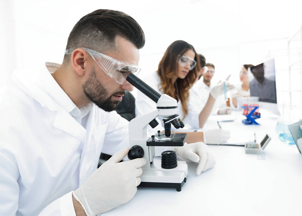 male lab technician looks at the sample under a microscope - Foto, immagini