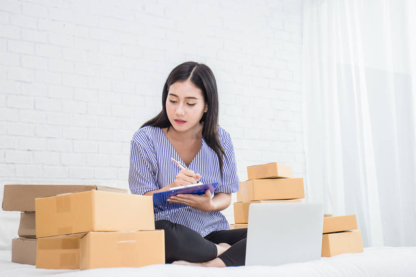 Young Asian small business owner sitting with laptop and boxes at home office - Φωτογραφία, εικόνα