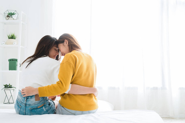 Back view of women lesbian happy couple waking up in morning, sitting on bed, stretching in cozy bedroom, looking through window. Funny women after wakeup. LGBT Lesbian couple together indoors concept - Photo, image