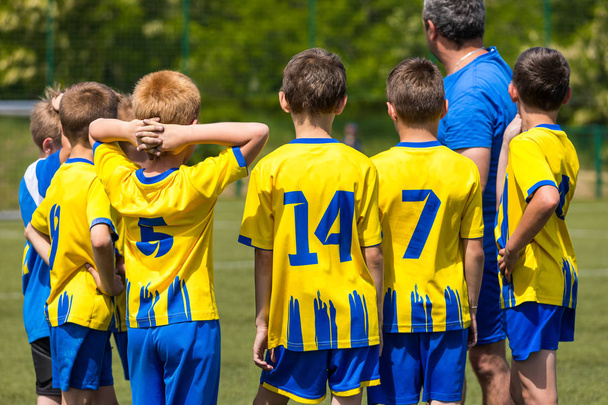 Lasten jalkapallojoukkue. Lapset seisovat yhdessä kentällä. Nuorten jalkapallovalmentaja motivoi pelaajia ennen ottelua. Jalkapallovalmentajan puhe
 - Valokuva, kuva