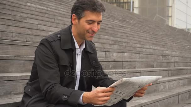 Lento movimento tutor de negócios do sexo masculino sentado em escadas e lendo jornais
. - Filmagem, Vídeo
