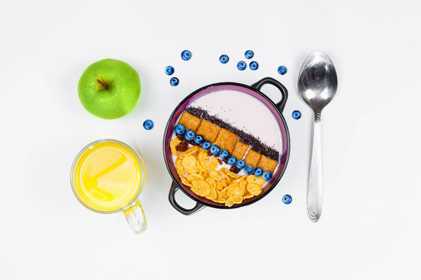 Breakfast, bowl with homemade yogurt and cornflakes, and fresh blueberries, a glass of orange juice, and a green apple on a white background, top view, flat lay. Concept of healthy food, healthy food, - Φωτογραφία, εικόνα