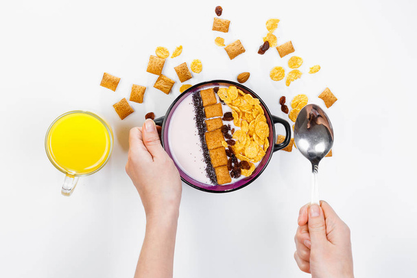 Morning breakfast. Female hands hold a spoon over a bowl with homemade yogurt and cornflakes, raisins, almonds on white background, top view, flat lay. Concept of healthy food, healthy food, detox. Co - Foto, afbeelding