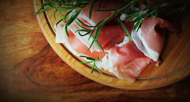 Prosciutto crudo italiano o jamón con romero sobre tabla de cortar
 - Foto, imagen