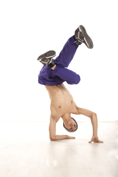 junger männlicher Tänzer sitzt auf Händen und führt Breakdance-Bewegungen vor - Foto, Bild